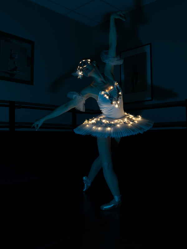 Female LED ballerina for events posing in dark studio with arms in air during photoshoot | Altus Entertainment